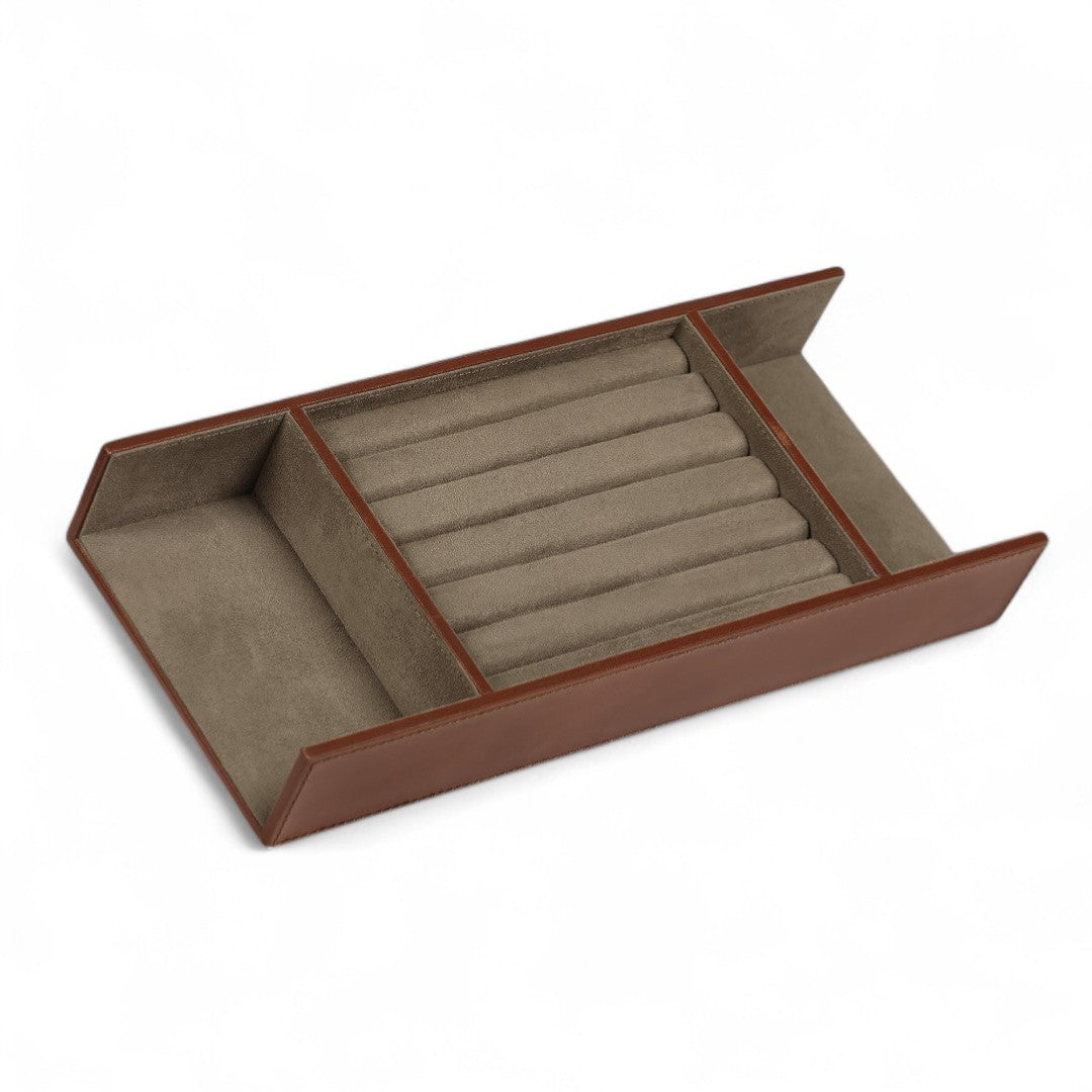 Jewelry tray with brown leather border and beige interior holding jewelry on a white background